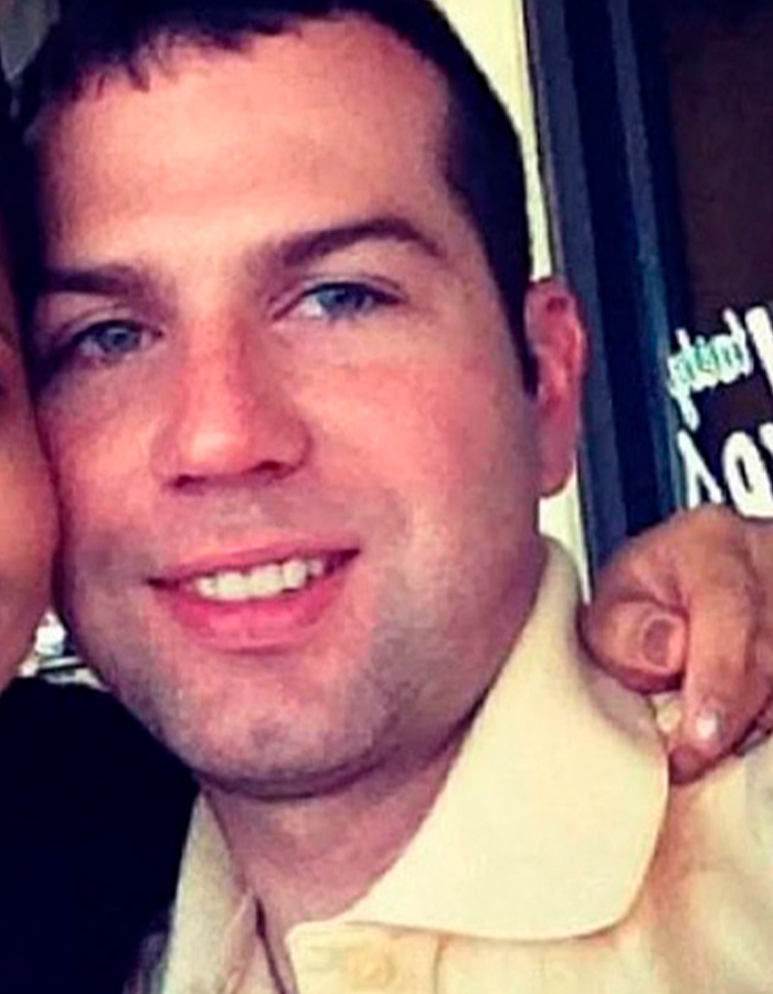 Close-up of a smiling man with blue eyes, wearing a light-colored shirt, relating to ICE agent fundraising controversy.