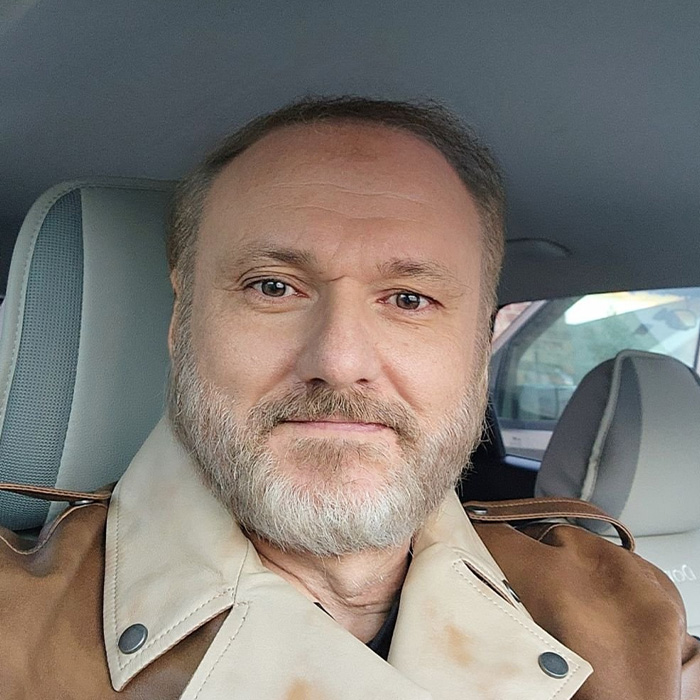 Man with beard and coat sitting in a car, related to ICE slammed for not letting detained father attend son's funeral.