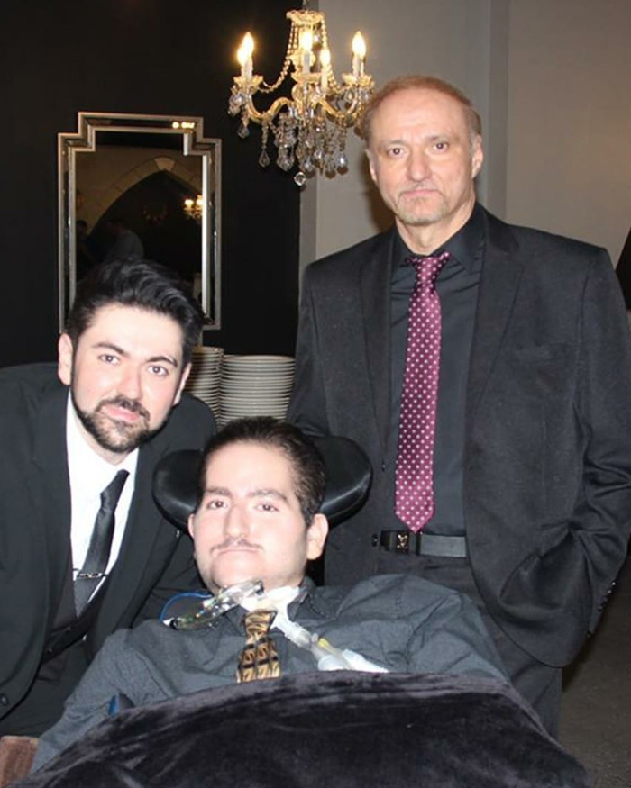 Three men dressed formally, including a man in a wheelchair, symbolizing detained father unable to attend son's funeral.