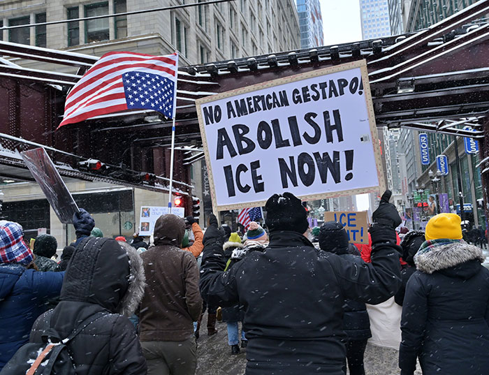 Protesters in winter coats hold signs calling to abolish ICE during a heated demonstration on a snowy city street. Protesters in winter coats hold signs calling to abolish ICE during a heated demonstration on a snowy city street.