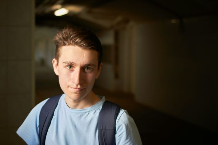 Teenage boy with backpack in a dimly lit hallway, representing high school life and its unexpected controversies.