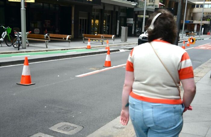 Street photographer captures perfect coincidences of urban life with a woman walking near traffic cones on the city street.