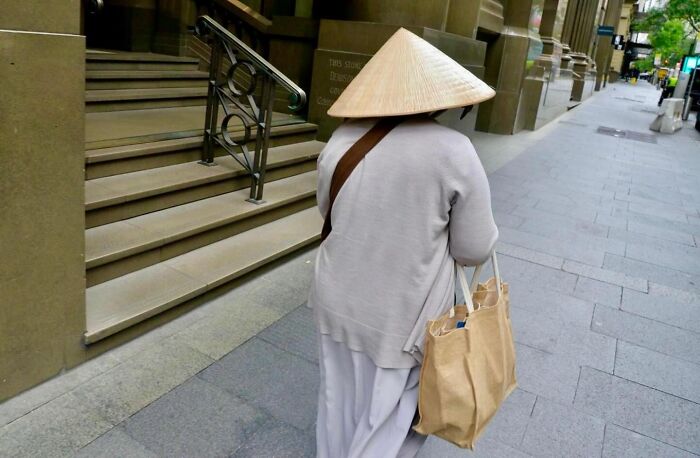 Street photographer captures perfect coincidences of a person wearing a conical hat walking down an urban sidewalk.