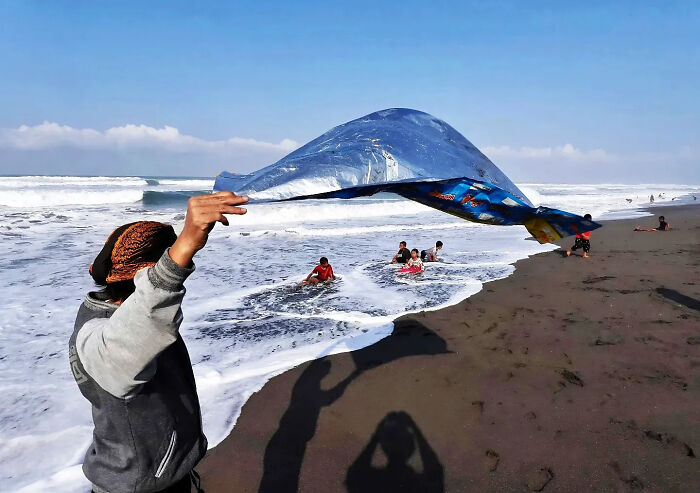 Photographer captures perfectly timed street shot at beach with person holding a tarp and children playing in ocean waves.