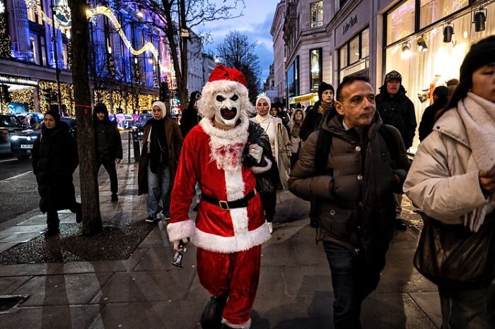 Candid street photo showing a person in a Santa costume with a mask among pedestrians, capturing humanity and absurdity.