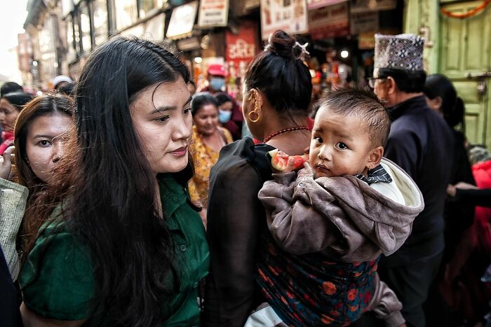 Candid street photo showing a woman holding a child in a busy market scene capturing humanity and tender moments.