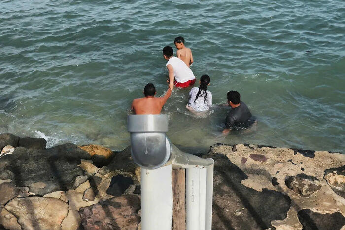 Four people wading in water near rocks, captured in a perfectly timed street shot by a photographer.