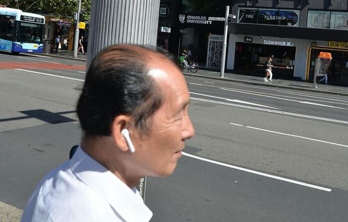 Man wearing wireless earbuds on city street, captured by street photographer known for perfect coincidences.