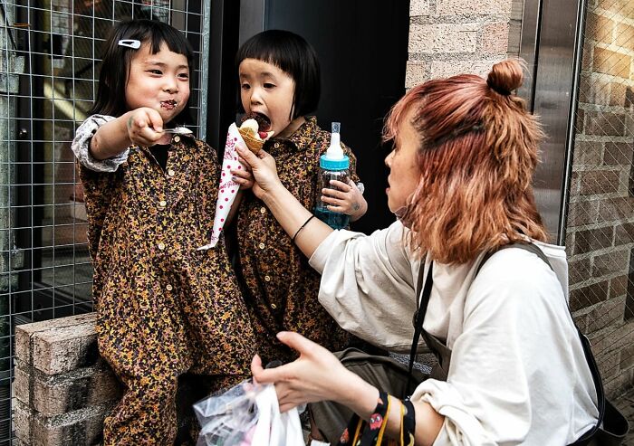 Candid street photo of a woman sharing ice cream with two children, capturing tender moments and humanity outdoors.