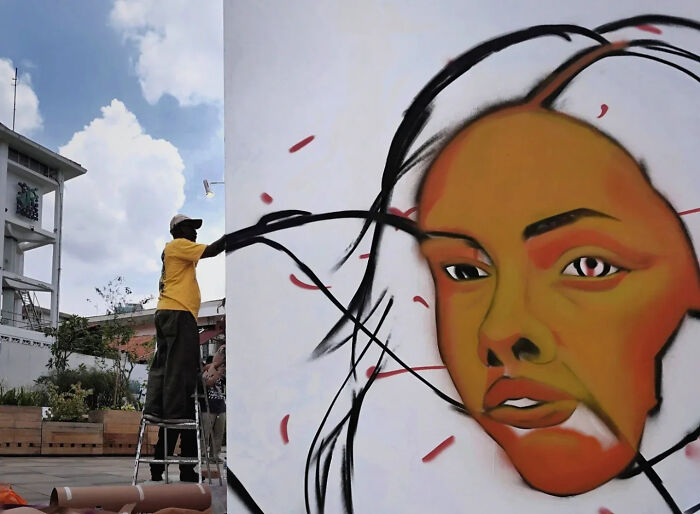 Photographer capturing perfectly timed street shot of an artist painting a large vibrant mural on an outdoor wall.