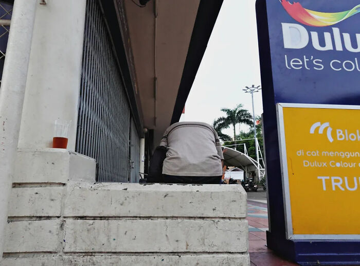 Perfectly timed street shot showing a person sitting next to urban signage in a busy outdoor setting.