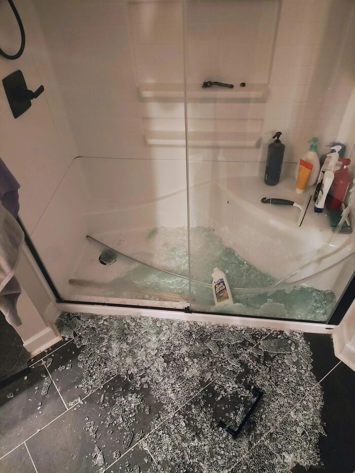 Broken glass shower door shattered on bathroom floor with shampoo bottles inside, showing unfortunate events that make you feel better.