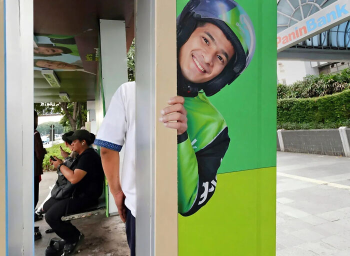Street shot capturing a person perfectly aligned with a smiling delivery rider poster, showcasing perfect timing photography.