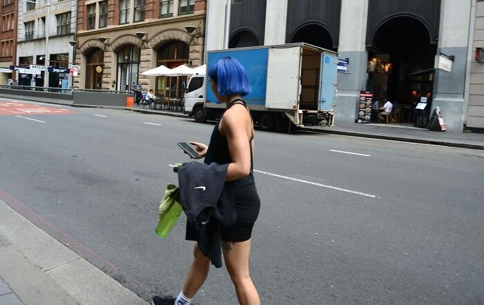 Street photographer capturing perfect coincidences of a woman with blue hair walking on an urban sidewalk.
