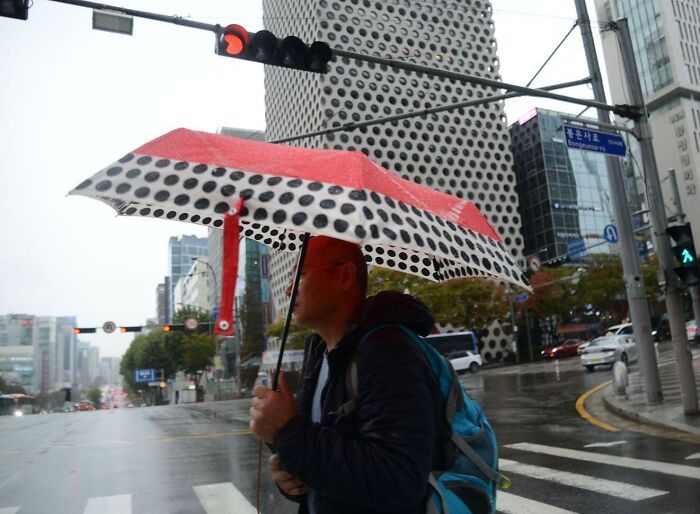 Man holding a polka dot umbrella perfectly aligned with a building pattern, capturing a street photography coincidence.