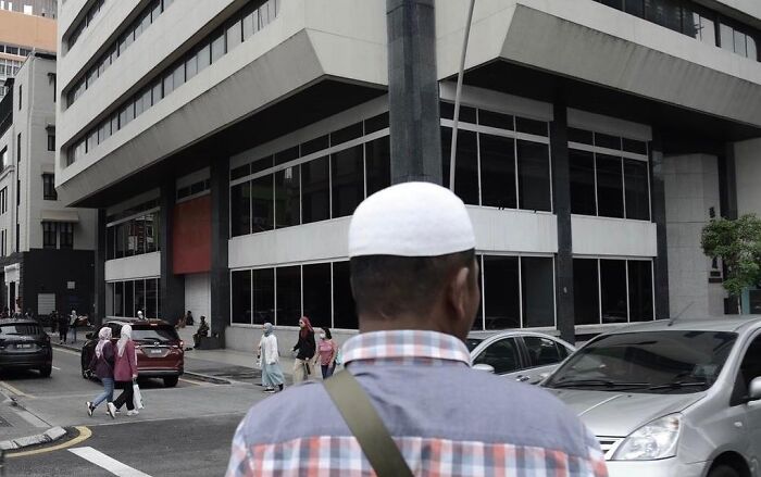 Man wearing a white cap and checkered shirt standing on a city street, showcasing street photographer’s talent for perfect coincidences.