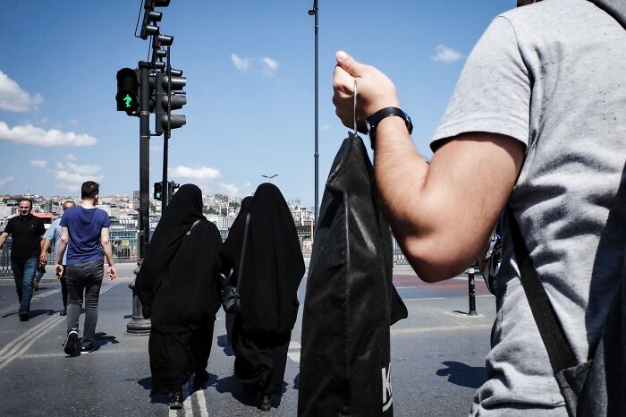 Street photo capturing diverse pedestrians crossing at a green light on a sunny day, showcasing life's unexpected moments.