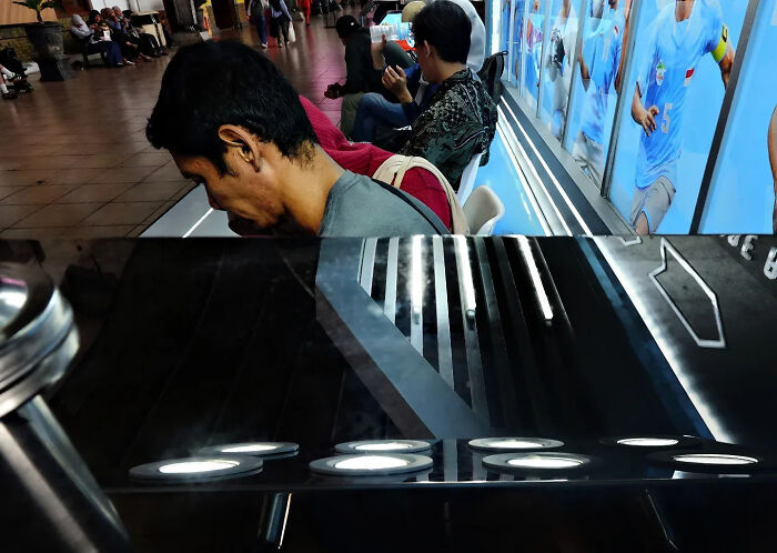 Man sitting indoors with reflective surfaces creating a perfectly timed street shot capturing unique visual reflections.