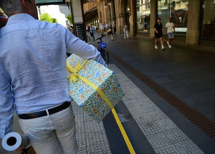 Street photographer capturing perfect coincidences as a man holds a gift box with a yellow ribbon on a busy city sidewalk.