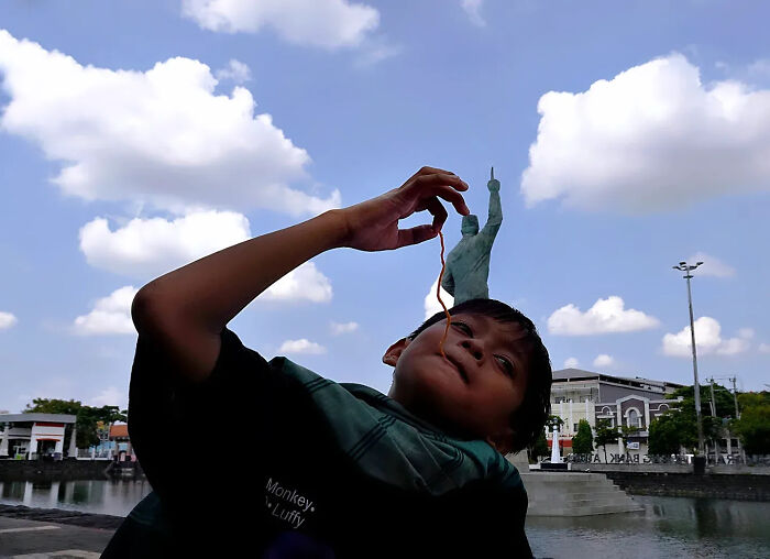 Boy eating noodle in front of a statue, a perfectly timed street shot capturing playful perspective and timing.