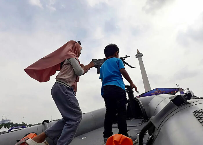 Two children playing on a military exhibit outdoors captured in a perfectly timed street shot near a city monument.