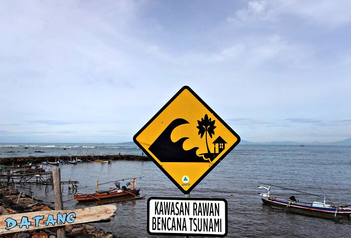Tsunami warning sign on a coastal street near boats, captured in a perfectly timed street shot by the photographer.