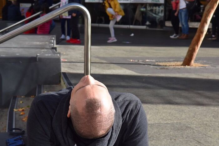 Street photographer captures a perfect coincidence of a man’s head aligned with a curved metal railing at the right moment.