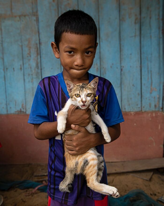 Boy holding a cat, capturing humanity and tender moments in a candid street photo with a rustic background.
