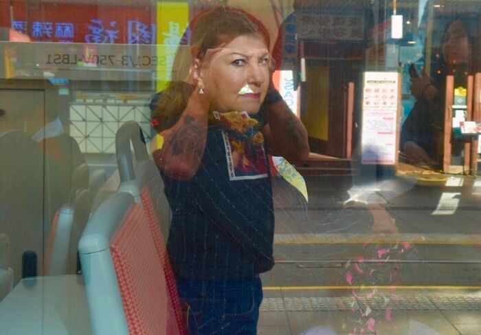 Street photographer captures perfect coincidence of a woman’s reflection blending with urban scene through a bus window.