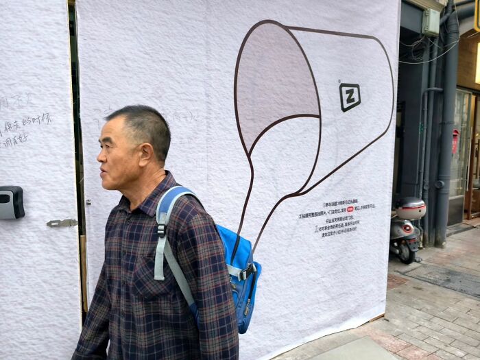 Man walking past street photo art of a tilted cup pouring liquid, capturing life’s unexpected and beautiful moments.