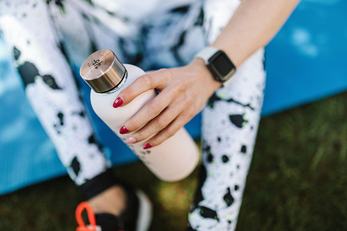 Woman holding water bottle on a yoga mat, wearing smartwatch and patterned leggings, hygiene mistakes adults