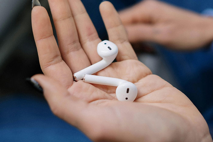 White wireless earbuds resting in open palm, highlighting hygiene mistakes from sharing or not cleaning earphones
