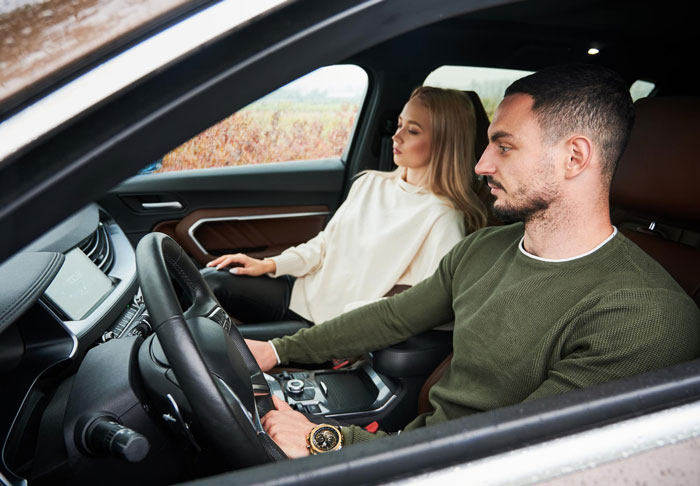 Couple sitting inside a car looking tense, illustrating SIL holding couple hostage and threatening to destroy car with food.