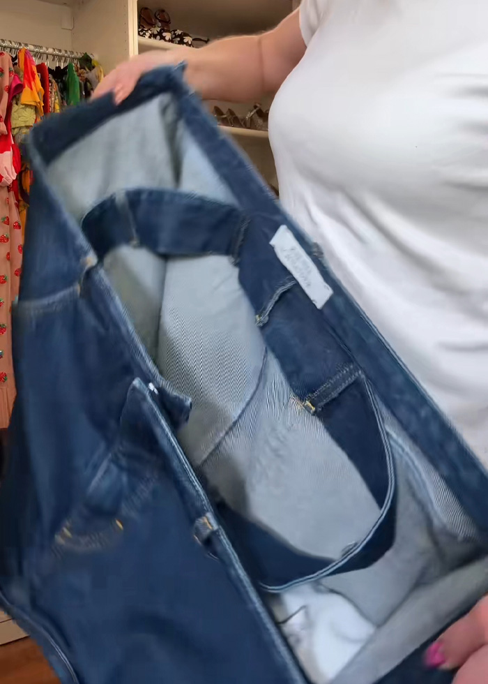 Person holding open a pair of cubic jeans, highlighting the unique boxy design and denim fabric in a wardrobe setting.