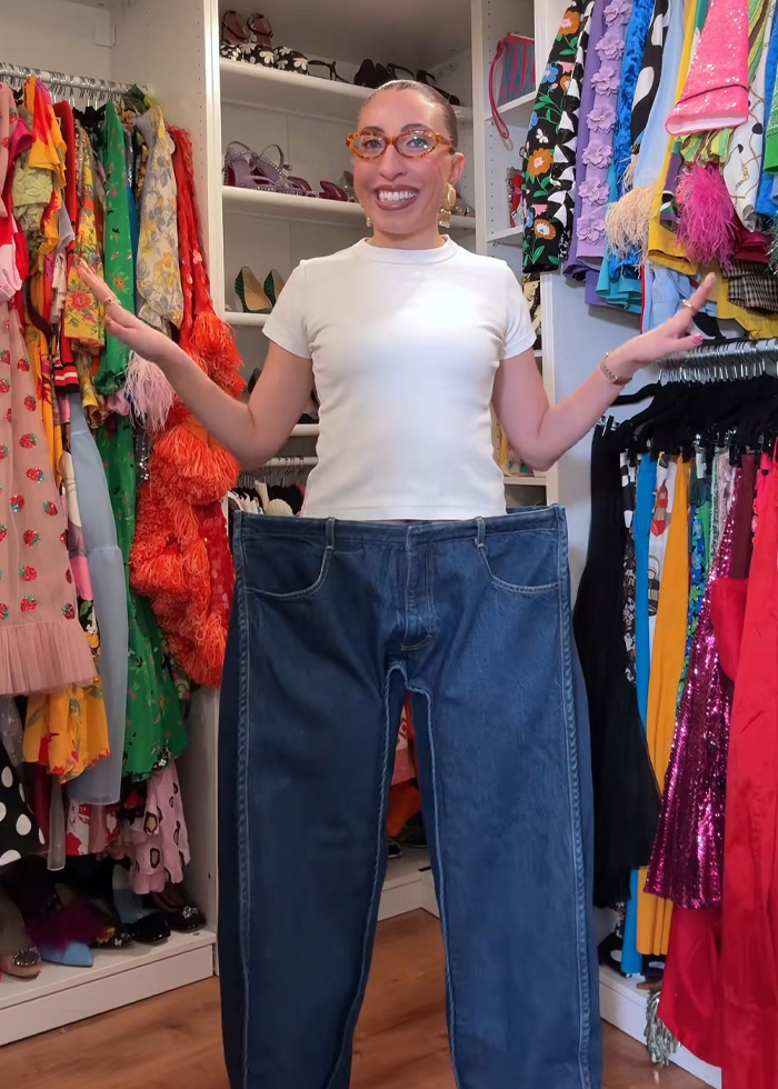 Influencer showcasing oversized cubic jeans in a colorful closet, sparking debate on social media fashion trends.