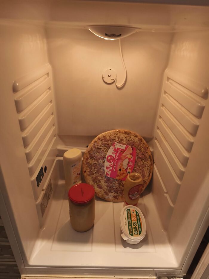 Open fridge with unusual and limited fridge contents including a pizza, jars, and bottles, showcasing interesting fridge contents.