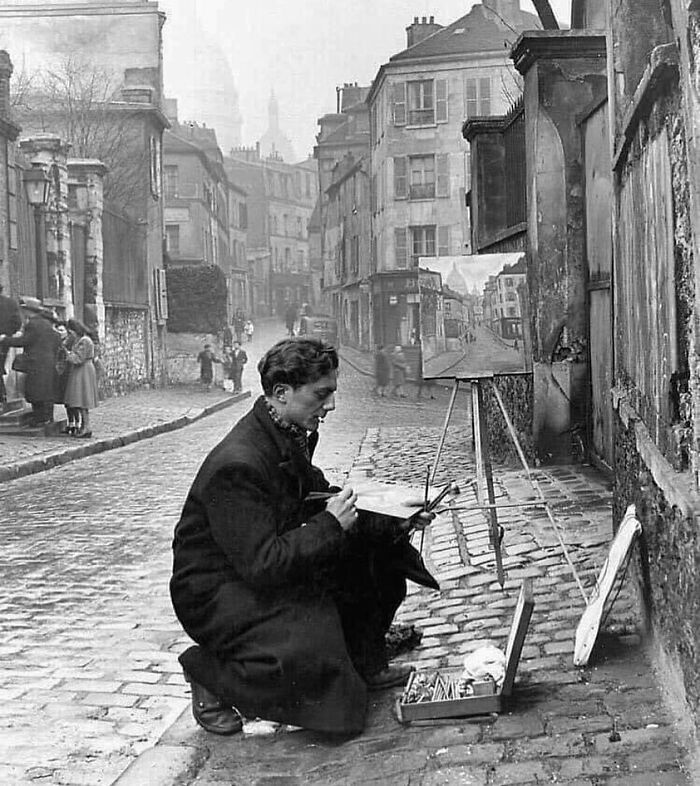 Black and white photograph of a man painting a street scene, capturing a moment in the history of humanity through art.