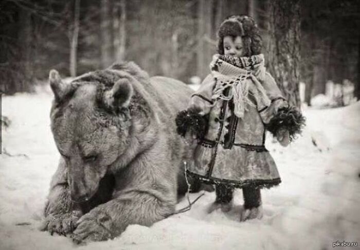 Child in winter clothing standing next to a large bear in a snowy forest, capturing a moment of history and humanity.