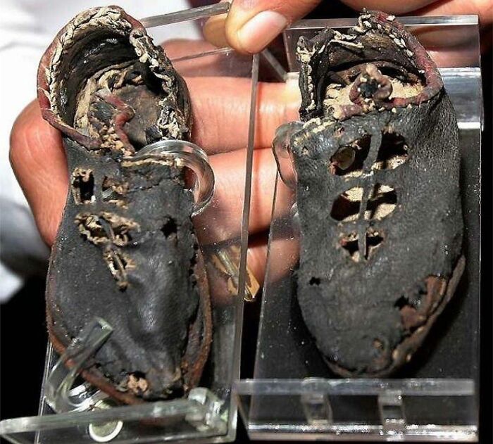 Worn and deteriorated ancient shoes held carefully on display, illustrating the sad and sometimes horrific history of humanity.