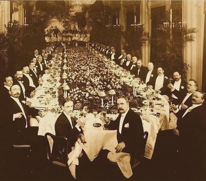 Vintage photograph of elegantly dressed men at a long banquet table, reflecting the complex history of humanity.