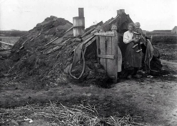 Black and white photograph of a family at the entrance of a sod house depicting history of humanity hardships.