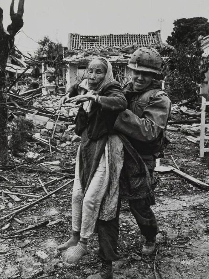 Soldier carrying elderly woman through ruins, capturing the sad, beautiful, and sometimes horrific history of humanity.