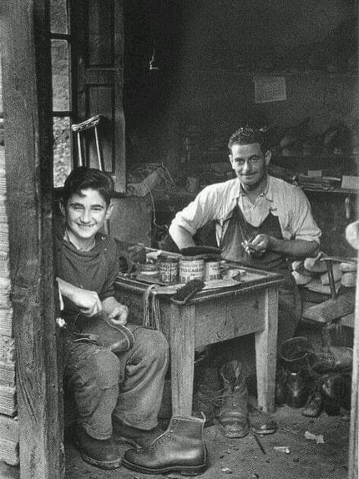 Two shoemakers working with tools and boots in a workshop, capturing the history of humanity through photography.