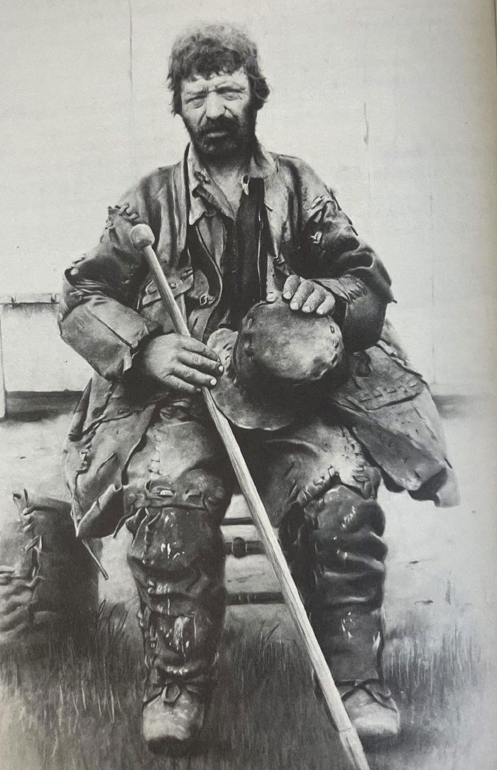 Black and white photo of a worn man in tattered clothes sitting with a cane, showcasing a hidden side of history.