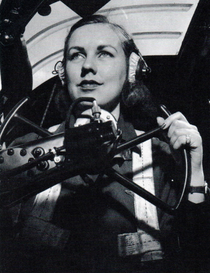 Female pilot wearing headset and gripping control wheel inside airplane cockpit in historical black and white photo.