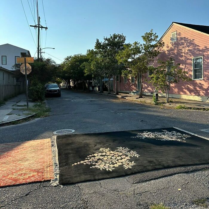 Two decorative rugs laid out on a street, one black with floral patterns, creating a weird street find scene.