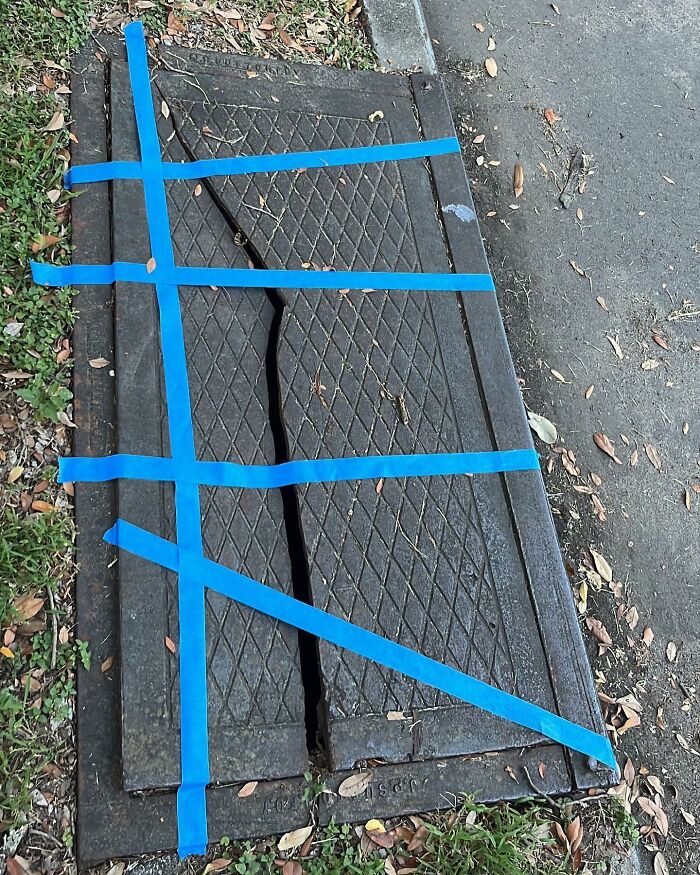 C*****d street metal hatch taped with blue strips, showing a weird find in the streets.