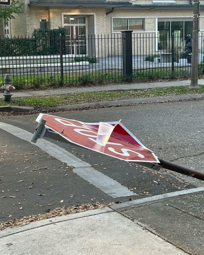 Bent stop sign lying on a street corner with a plastic cup placed on top, one of the weirdest things found in the streets.