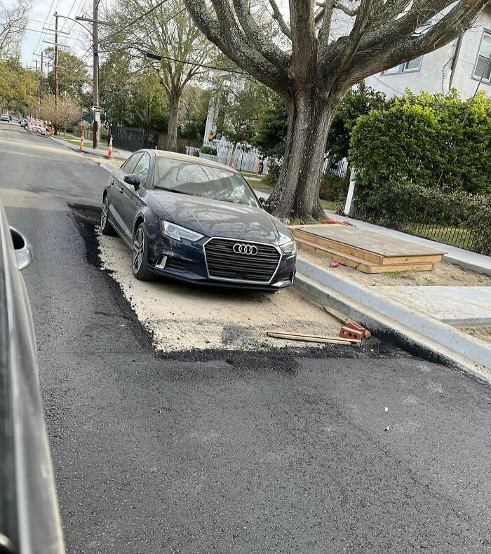 Black Audi parked in the middle of a street patch, surrounded by fresh asphalt and construction debris.