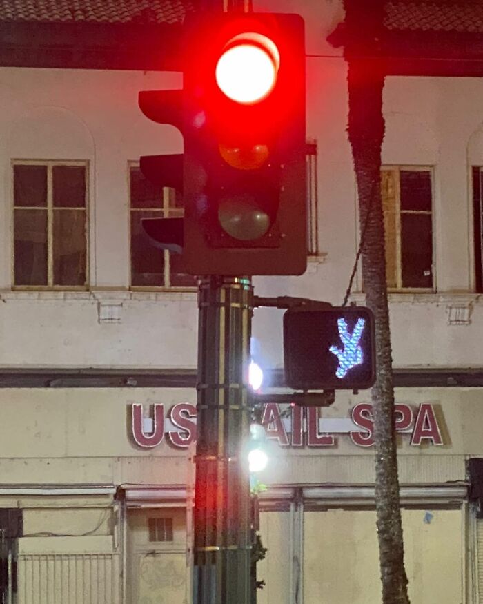 Traffic light showing red while pedestrian signal displays an unusual peace hand sign on the street.